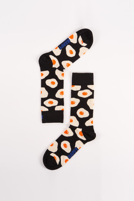 Chaussettes noires avec imprimé d'œuf au plat de Happy Socks, bord rayé et logo bleu sur les orteils, posées à plat sur fond blanc