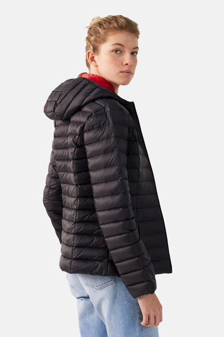 Vrouw met zwarte gewatteerde jas met capuchon en blauwe spijkerbroek.