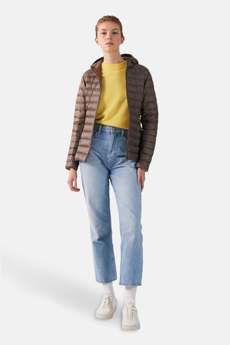 Vrouw in pufferjack, gele trui, jeans en witte sneakers.