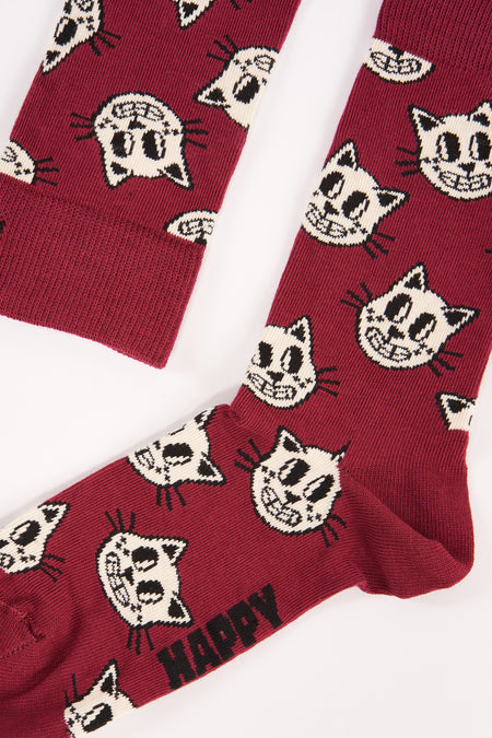 Chaussettes rouge foncé avec imprimé de petits chats blancs de Happy Socks, rayées et avec le texte "HAPPY" sur la semelle, posées à plat sur fond blanc.