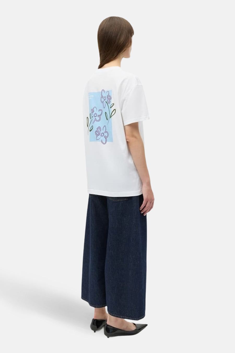 T-shirt blanc à manches courtes d'ENVII, avec imprimé floral au dos, associé à un jean ample bleu foncé et des chaussures noires.