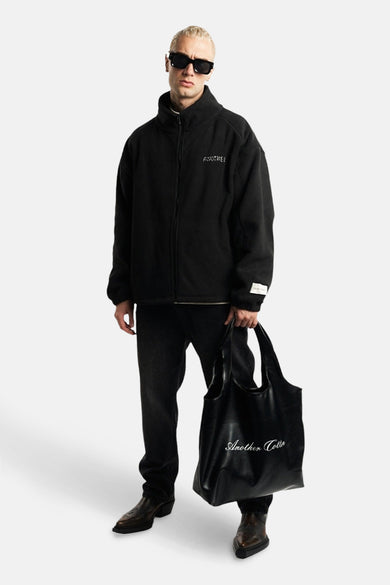 Veste noire d'ANOTHER COTTON LAB, portée avec un sac à dos noir et des jeans foncés.