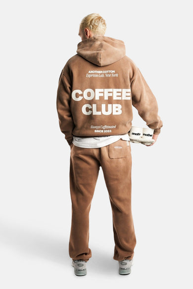 Pull-over marron avec capuche d'ANOTHER COTTON LAB, avec une impression de texte blanche sur le dos, porté avec un pantalon coordonné.