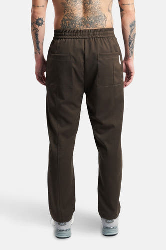 Pantalon brun de ANOTHER COTTON LAB, avec des poches sur le dos et porté avec des baskets grises.