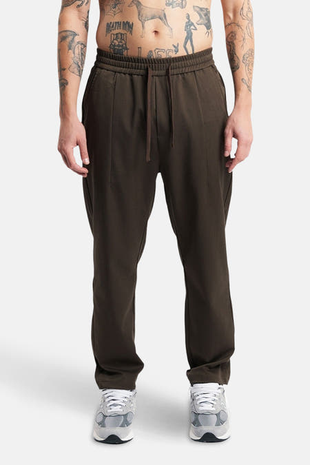Pantalon brun de ANOTHER COTTON LAB, avec cordon et porté avec des baskets grises.