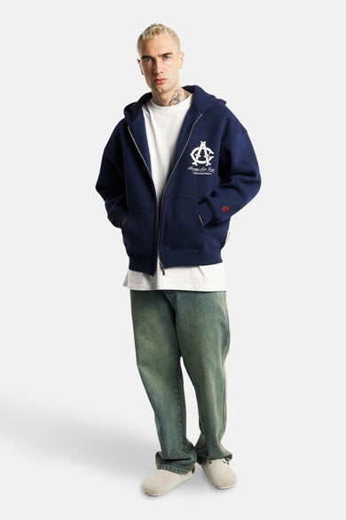 Pull-over bleu avec capuche d'ANOTHER COTTON LAB, imprimé de blanc, porté avec un T-shirt blanc et des jeans verts.