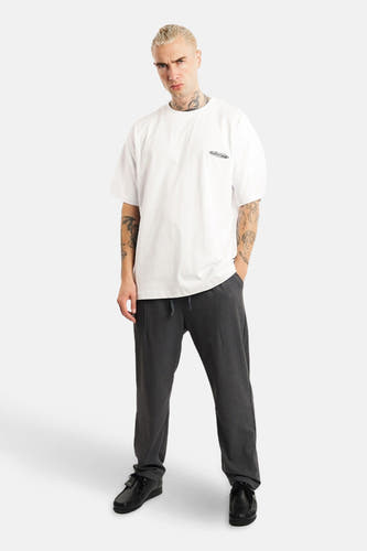 T-shirt blanc à manches courtes d'ANOTHER COTTON LAB, avec un petit logo, associé à des pantalons de jogging gris et des chaussures noires.