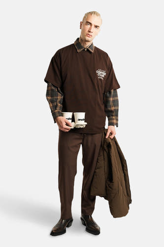 T-shirt brun à manches courtes d'ANOTHER COTTON LAB, porté sur un chemisier rayé, avec une tasse de café à la main.