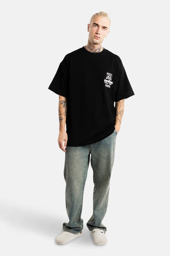 T-shirt noir à manches courtes d'ANOTHER COTTON LAB, avec une impression sur la poitrine, porté avec un jean et des mocassins blancs.