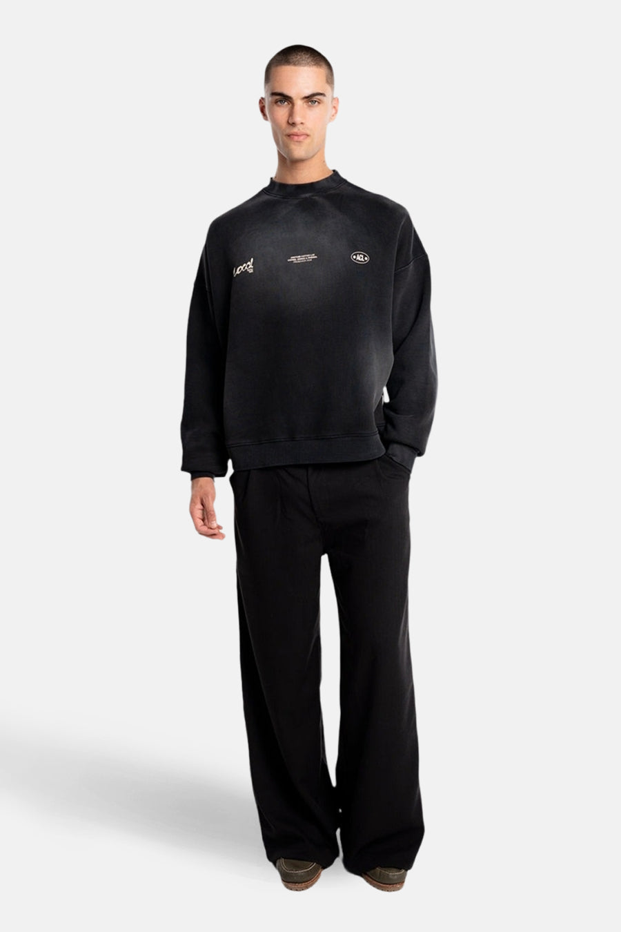 Pull noir de ANOTHER COTTON LAB, avec inscriptions et porté avec un pantalon noir ample.