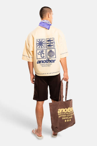 Geel korte mouwen overhemd van ANOTHER COTTON LAB, achterzijde met grafisch print, model draagt donkere korte broek en bruine tas