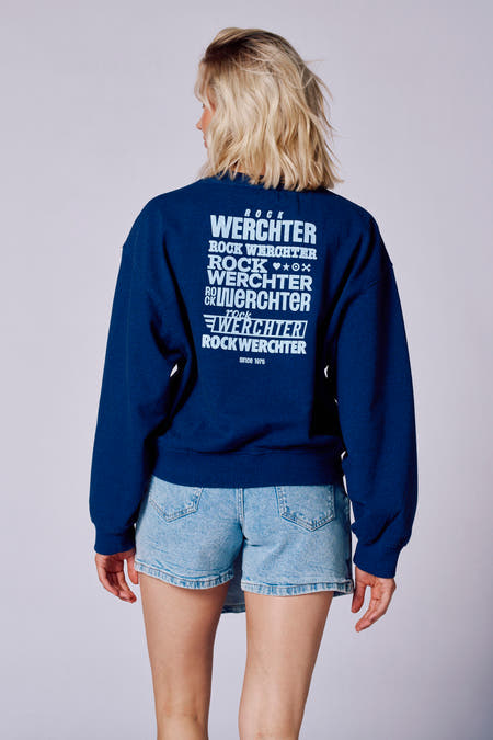 Gilet bleu avec col rond de Rock Werchter 50, porté avec une jupe en denim et des bottes noires.