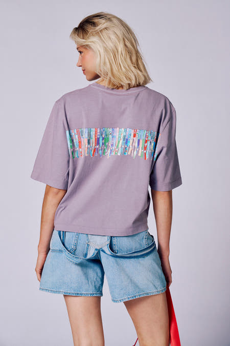 T-shirt violet à manches courtes de Rock Werchter 50, porté avec un pantalon en denim et des baskets crème.