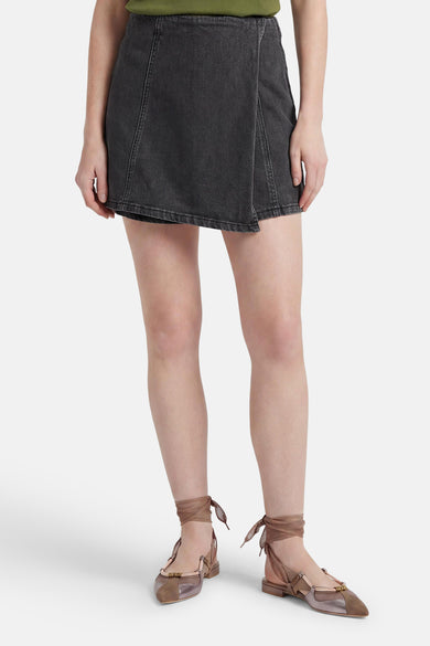 Zwarte denim skort van HAILYS met overslag, zichtbare naden, gecombineerd met een groene top en veterschoenen.