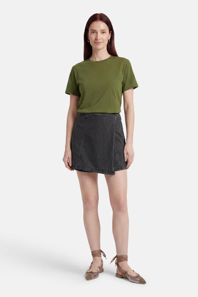 Skort en denim noir de HAILYS avec détail croisé, porté par un mannequin avec un t-shirt vert et des chaussures plates.