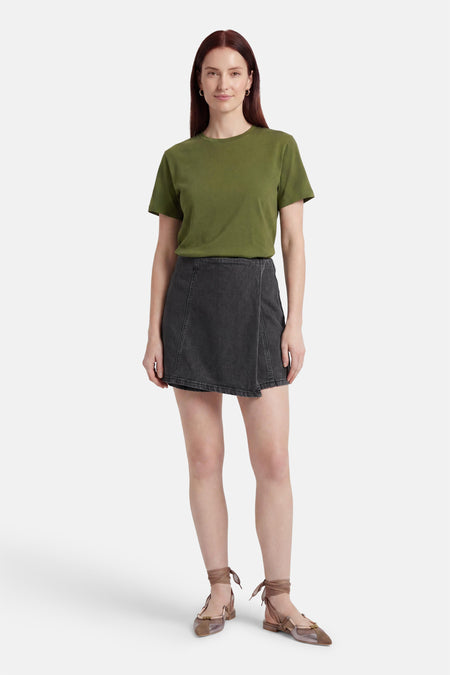 Skort en denim noir de HAILYS avec détail croisé, porté par un mannequin avec un t-shirt vert et des chaussures plates.
