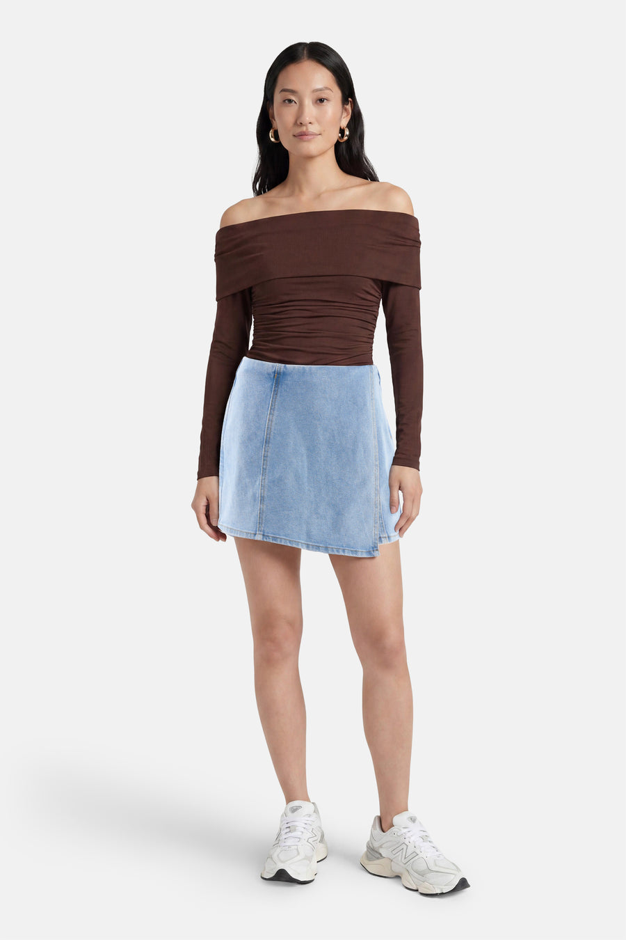 Skort en denim bleu clair de HAILYS avec une coupe trapèze, porté avec un haut marron épaules dénudées et des baskets blanches.