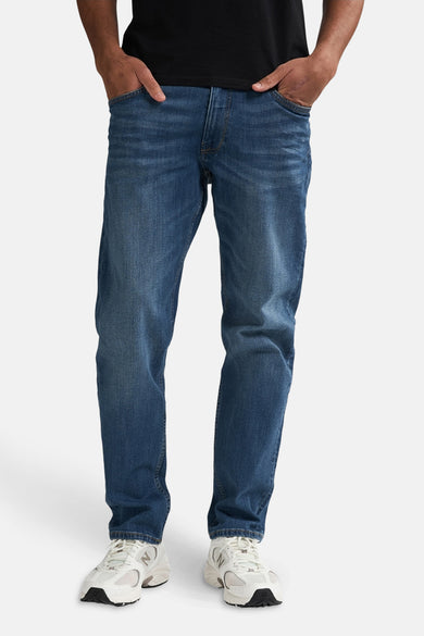 Boutons de fermeture éclair sur des jeans en denim bleu marine de Petrol Industries, avec deux mains dans les poches et des baskets blanches.