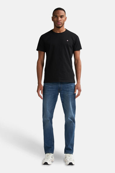 Jean tapered bleu de Petrol Industries, associé à un T-shirt noir et des baskets blanches.