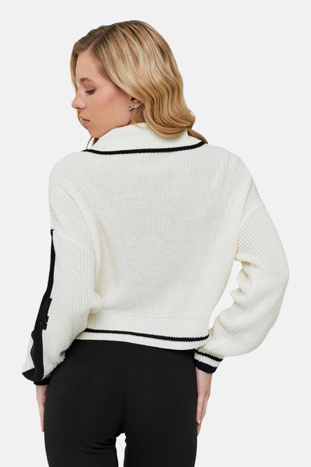 Achterkant van een blonde vrouw met een gebroken witte trui met zwarte accenten.