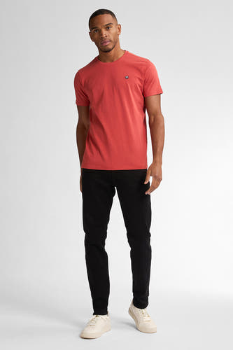 Jean slim fit noir de Petrol Industries, porté avec un t-shirt rouge et des baskets crème.