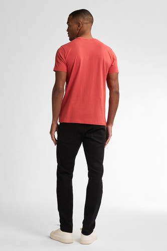 Zwarte slim-fit jeans van Petrol Industries, gezien vanaf de achterkant, gecombineerd met een oranje T-shirt en crèmekleurige schoenen.