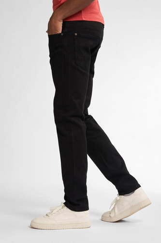 Jean slim noir de Petrol Industries, avec une main dans la poche et associé à des baskets crème.