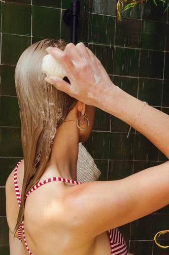 Multicolor douchegel van WONDR CARE, gebruikt in de douche door een vrouw in een rood-wit gestreepte top.