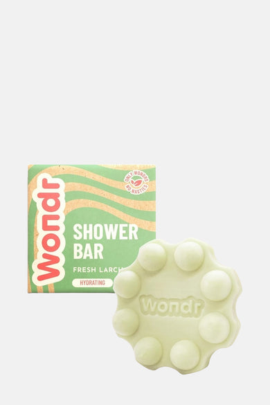 Douche verte de WONDR CARE sur un support vert avec une pierre blanche et une plante en premier plan.