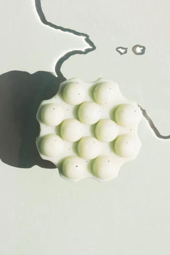 Produit de soin multicolore de WONDR CARE, avec des formes rondes et de petits points noirs, avec un ombre sur un fond vert.