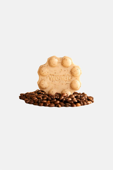 Gel douche solide beige avec des paillettes et un design pop-it de WONDR CARE, avec relief 'Wondr', debout sur des grains de café.