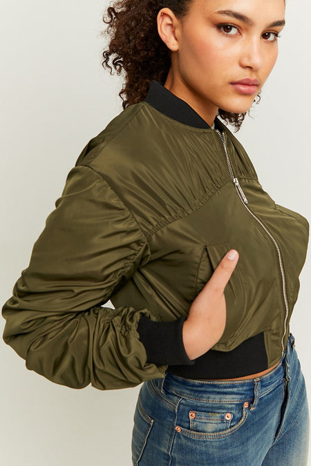 Manteau court vert de TALLY WEIJL, avec une fermeture éclair et porté avec un jean bleu.