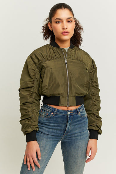 Manteau court vert de TALLY WEIJL, avec des manches froncées et une fermeture éclair argentée, porté avec un jean bleu.