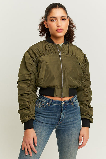 Manteau court vert de TALLY WEIJL, avec des manches froncées et une fermeture éclair argentée, porté avec un jean bleu.