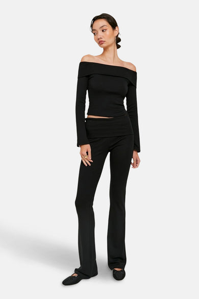 Pantalon noir de TALLY WEIJL, avec des jambes fuselées et porté avec un haut noir à épaules dénudées.