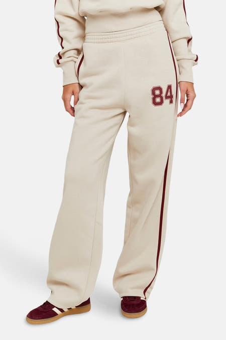 Jean de jogging beige TALLY WEIJL, avec un détail brodé '84' et des rayures bordeaux le long des côtés.