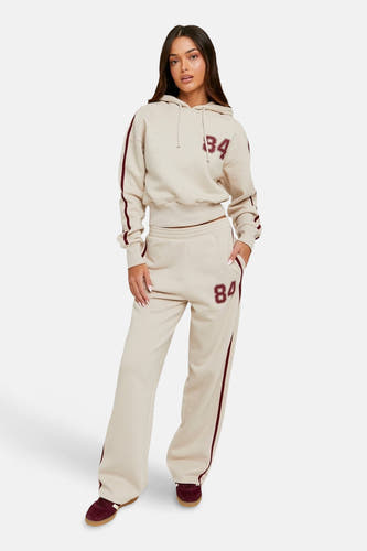 Jean de jogging beige TALLY WEIJL avec une bande rouge bordeaux et un numéro, associé à une hoodie correspondante et des chaussures.