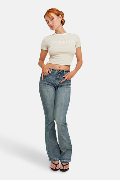 Jean bootcut bleu moyen de TALLY WEIJL, porté avec un t-shirt court et des sandales.