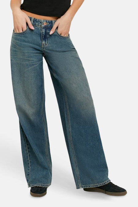Jean bleu clair à jambes larges de TALLY WEIJL, porté avec les mains dans les poches, un crop top noir et des baskets foncées.