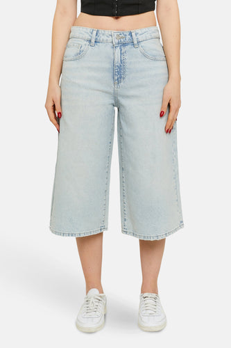 Vrouw in wijde, lichtblauwe jeansbroek met witte sneakers.