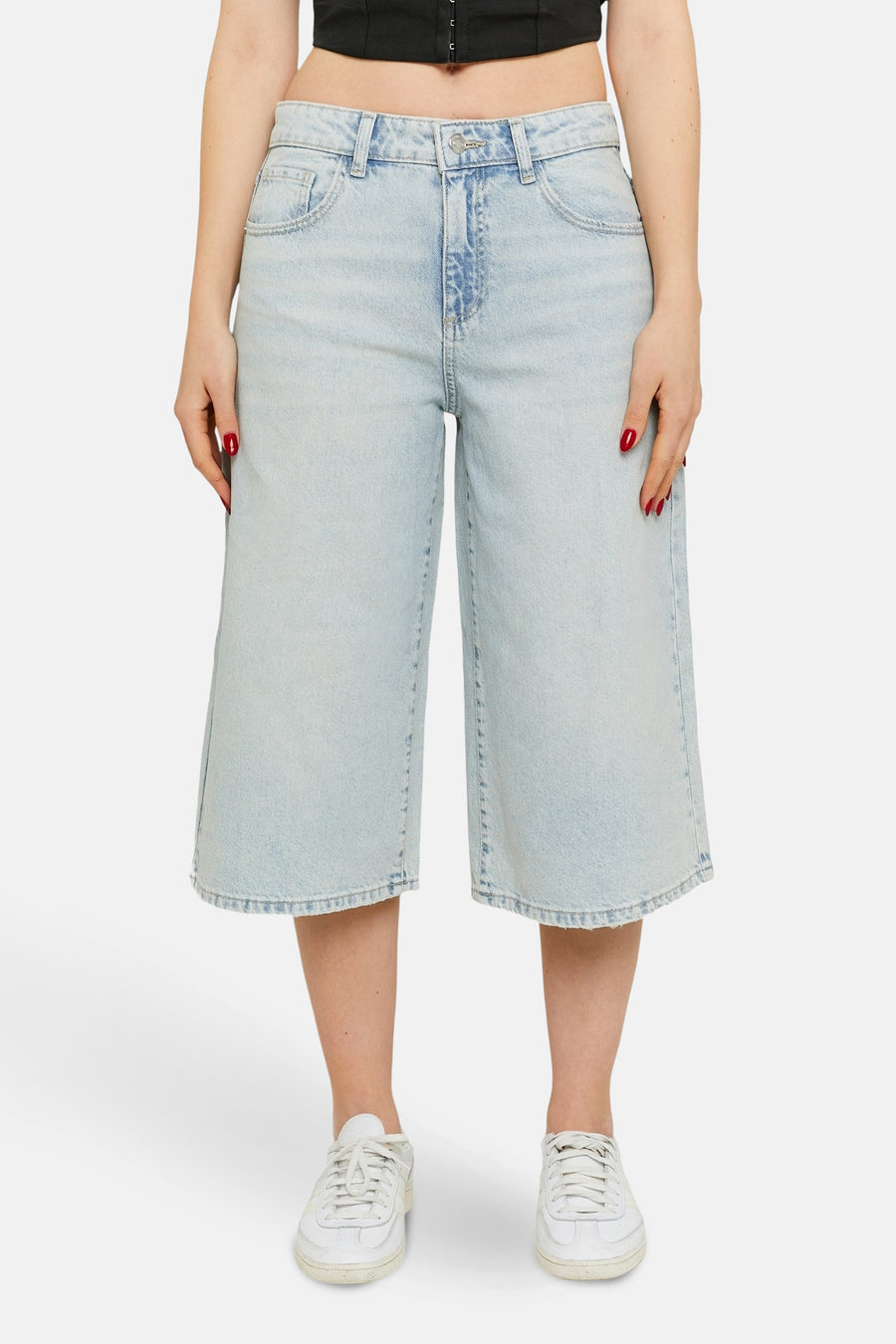 Vrouw in wijde, lichtblauwe jeansbroek met witte sneakers.