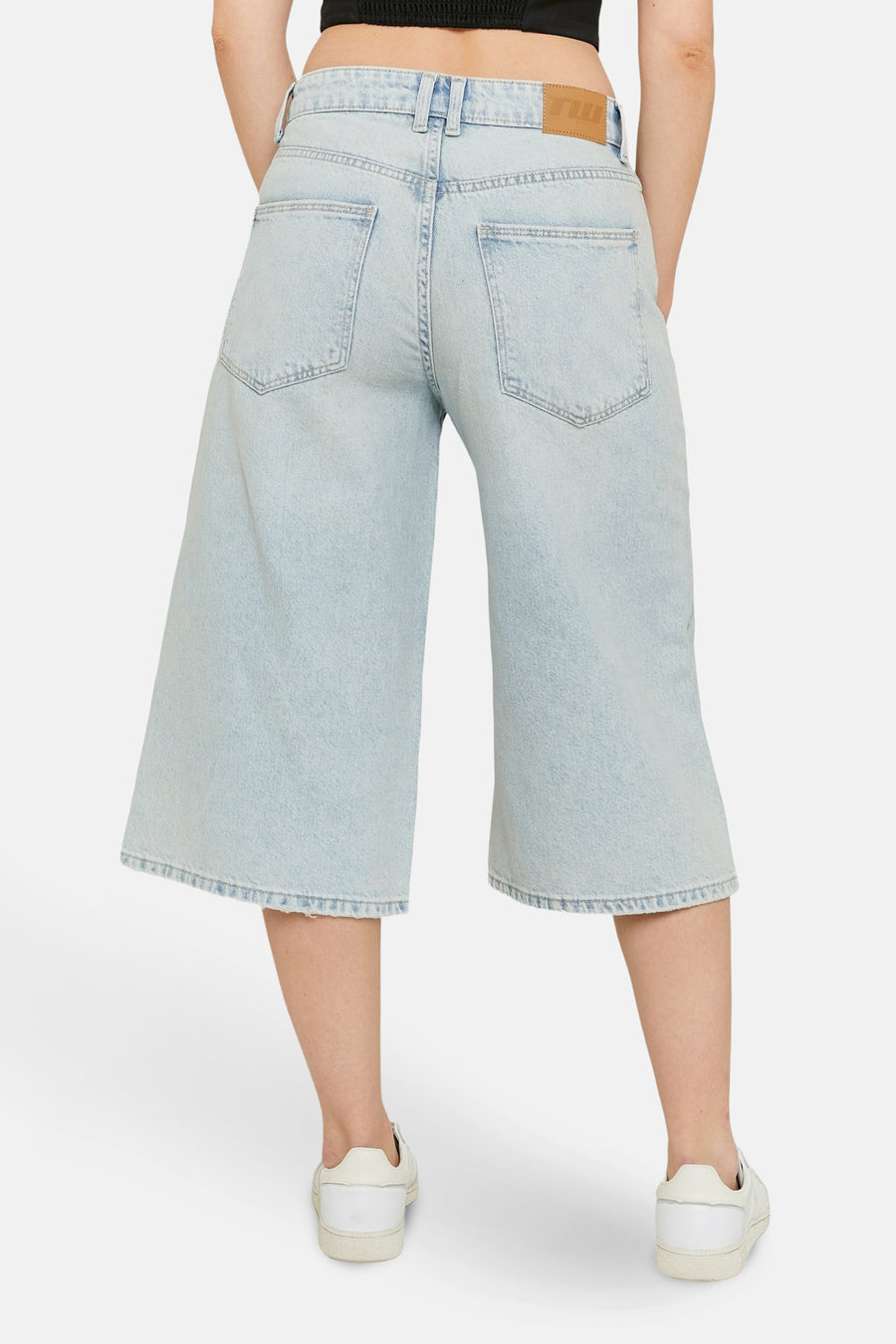 Achterkant van een persoon met wijde, lichtblauwe jeans en witte sneakers.