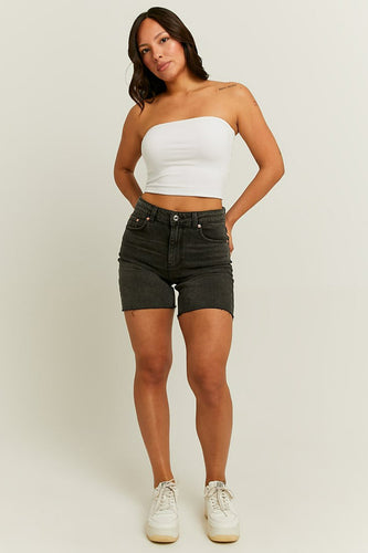Vrouw in witte strapless top, grijze denim shorts en witte sneakers.