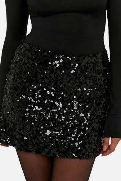 Jupe courte noire de TALLY WEIJL, recouverte de paillettes brillantes et associée à un pull manches longues noir.