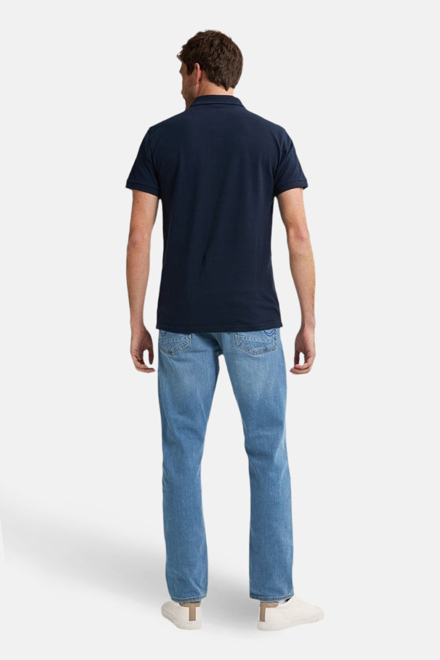 Man, achterkant, marineblauwe polo, jeans, witte schoenen.
