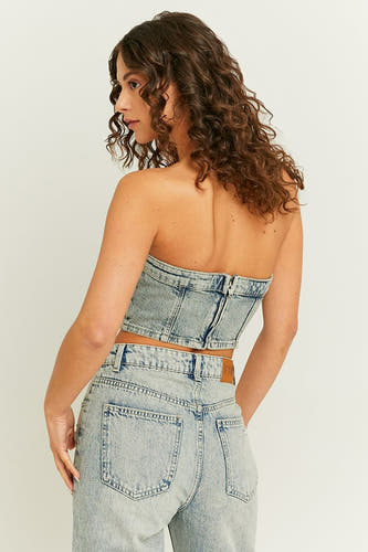 Blouse en denim bleu clair sans manches de TALLY WEIJL, avec fermeture à glissière à l'arrière, associée à des jeans.