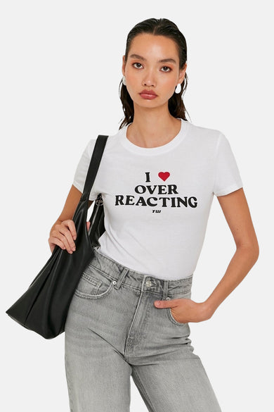 T-shirt blanc à manches courtes de TALLY WEIJL, avec du texte noir et un cœur rouge, associé à des jeans gris et une sac noir.