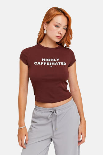 T-shirt brun à manches courtes de TALLY WEIJL, avec le texte "Highly Caffeinated" et associé à un short de jogging gris.
