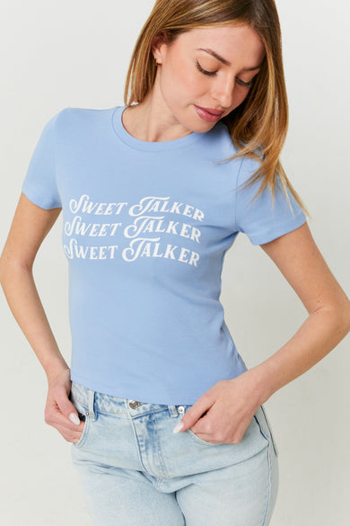 T-shirt bleu à manches courtes de TALLY WEIJL, avec une impression de texte "Sweet Talker" blanche, porté avec un jean.