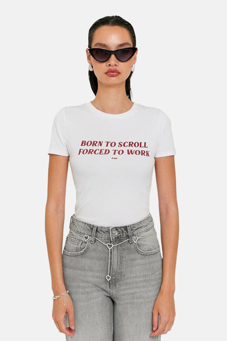 T-shirt blanc à manches courtes de TALLY WEIJL, avec le texte rouge "Born to scroll forced to work", associé à un jean gris et des accessoires argentés.